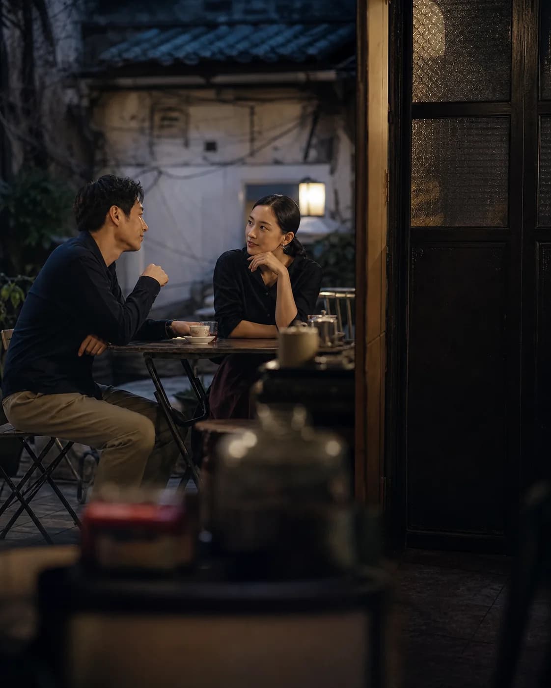 Two Hong Kong adults talk attentively at a cafe; a brand scene, not real members.