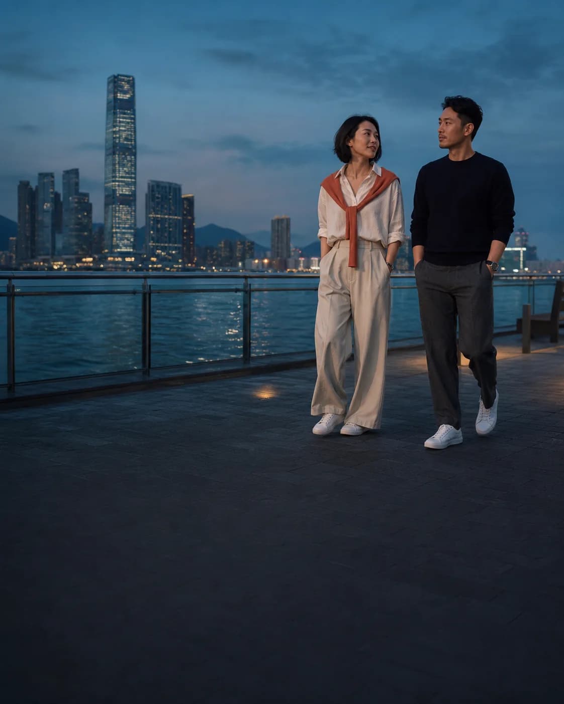 Two Hong Kong adults walk beside Victoria Harbour at dusk; a brand scene, not real members.
